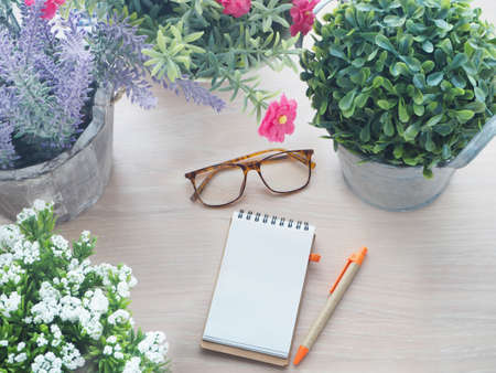 wood table with beautiful flower frame on pot and blank screen for text on notepad paper and modern eyeglasses, view from top wood table.の写真素材
