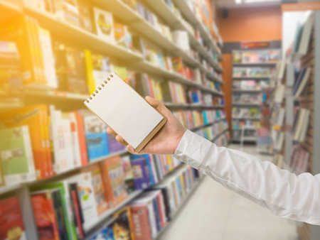 human hand hold blank screen on notebook paper on book store background.の写真素材