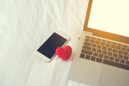 white bed with blank screen on smartphone, tablet, cell phone and red heart shape sign.の写真素材