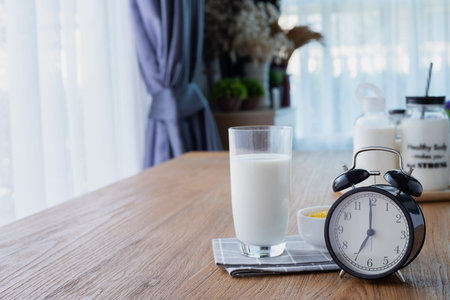 wood table with glass of milk and retro alarm clock in living room. front view table.
