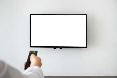human hand pressing remote control with blank screen television on concrete wall at living room. copy space for text on TV.の写真素材