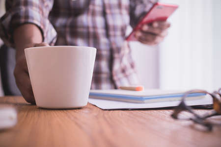businessman using smartphone and drink coffee. selective focus on coffee cup.の写真素材
