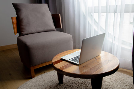 wooden table with laptop and modern chair in living room, morning light.