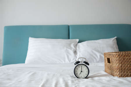classic clock on white bed with wooden basket on bed in bedroom, front view.の写真素材
