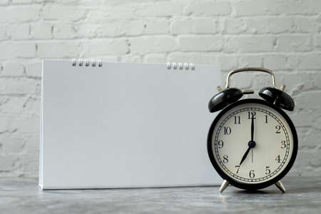 Classic clock with blank calendar note on brickwall background, view from front table.の写真素材