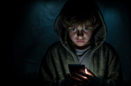 Terrified 7-year-old in dark room with mobile phoneの素材