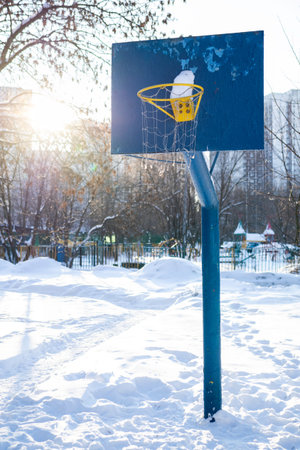 A snow-covered basketball hoop in a snowy urban park on a bright winter day
