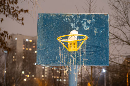 A basketball hoop covered with snow at night with a blurred urban background