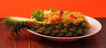 seafood and baked rice in pineapple with an orange background on a wood tableの写真素材