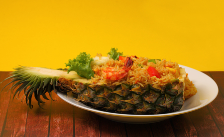 seafood and baked rice in pineapple with a yellow background on a wood tableの写真素材
