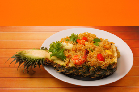 seafood and baked rice in pineapple on a wood table with an orange backgroundの写真素材