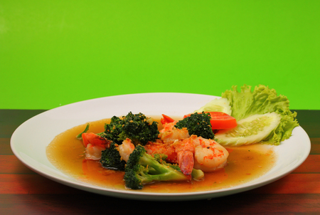 Shrimp and broccoli stir fry in sauce with a green background on a wood tableの写真素材