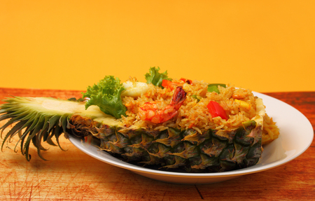 seafood and baked rice in pineapple with a yellow background on a wood tableの写真素材