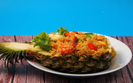 seafood and baked rice in pineapple with a blue background on a wood tableの写真素材