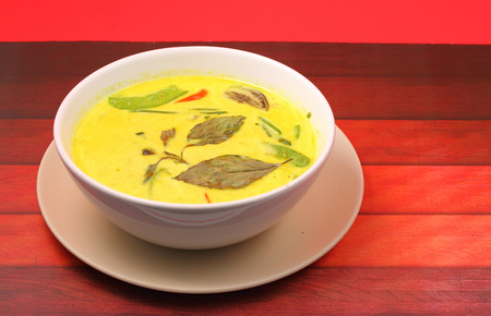 Hot and spicy chicken green curry on a red background on a wood table topの写真素材