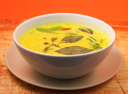 Hot and spicy chicken green curry on an orange background on a wood table topの写真素材