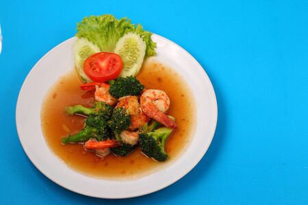 Shrimp and broccoli stir fry in sauce with a blue backgroundの写真素材