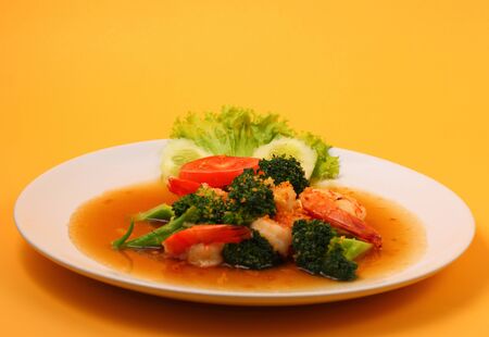 Shrimp and broccoli stir fry in sauce with an orange backgroundの写真素材
