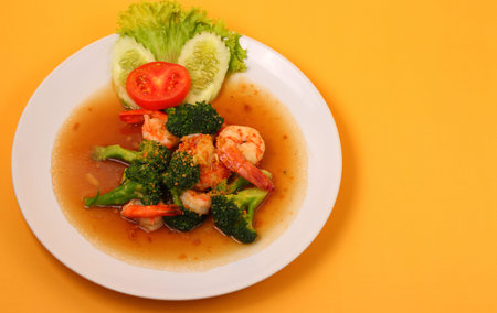 Shrimp and broccoli stir fry in sauce with an orange backgroundの写真素材