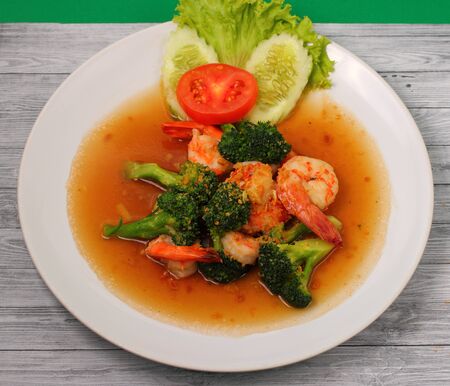 Shrimp and broccoli stir fry in sauce with a green background on a wood tableの写真素材