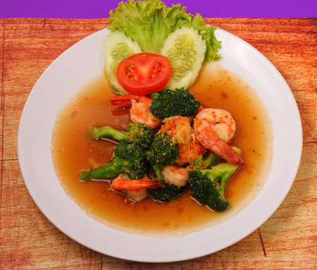 Shrimp and broccoli stir fry in sauce with a purple background on a wood tableの写真素材
