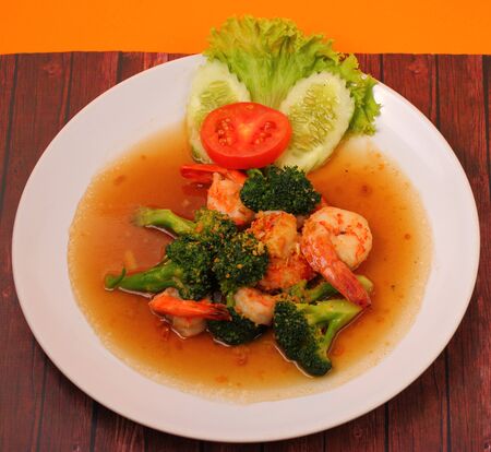 Shrimp and broccoli stir fry in sauce with an orange background on a wood tableの写真素材