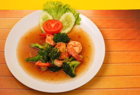 Shrimp and broccoli stir fry in sauce with a yellow background on a wood tableの写真素材