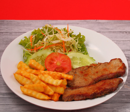 Grilled beef and french fries thai style with a red background on a wood table topの写真素材