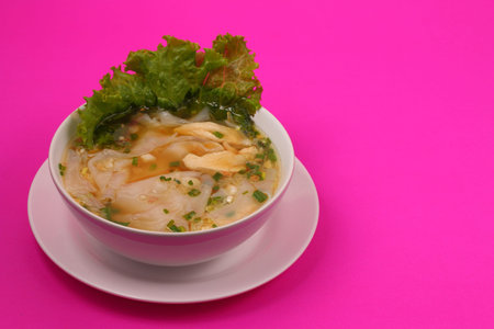 Glass noodle soup with chicken and beansprouts on a pink backgroundの写真素材