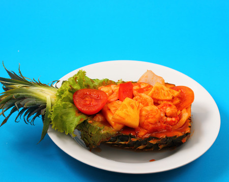 sweet and sour shrimp served in a pineapple thai style with a blue backgroundの写真素材