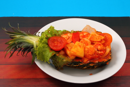sweet and sour shrimp served in a pineapple thai style with a blue background on a wood table topの写真素材