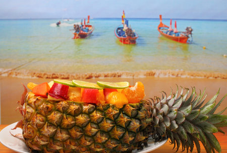 Thai style fruit salad inside a pineapple with a beach background on a wood table top