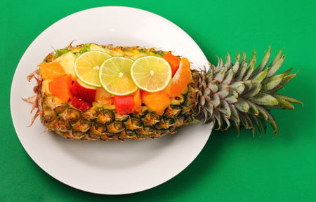 Thai style fruit salad inside a pineapple with a green backgroundの写真素材