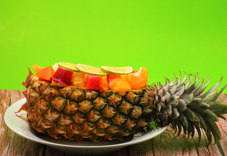 Thai style fruit salad inside a pineapple with a green background on a wood table topの写真素材