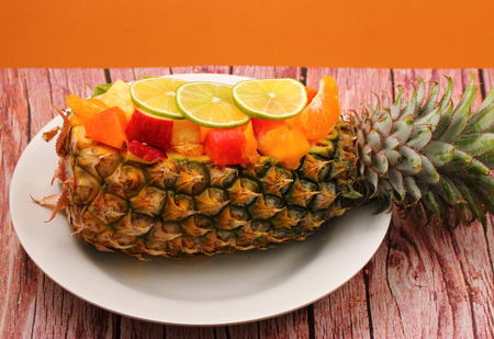 Thai style fruit salad inside a pineapple with a brown background on a wood table topの写真素材