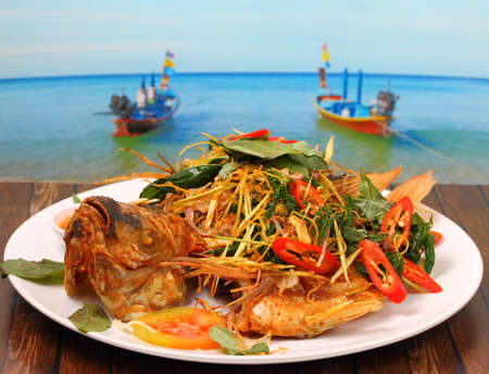 thai style fried fish with herbs on a wood table on the beachの写真素材