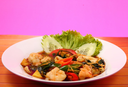 thai style seafood stir fry with a pink background on a wood table topの写真素材