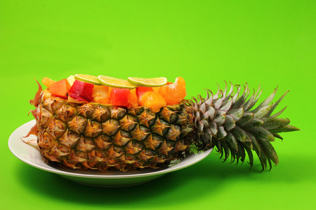 Thai style fruit salad inside a pineapple with a green backgroundの写真素材