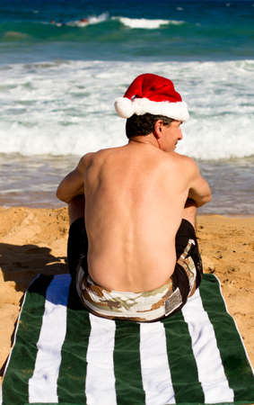 Man sitting on the beach in Hawaii wearing a Santa Hatの写真素材