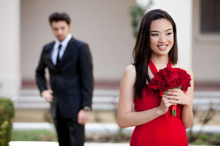 Beautiful Asiian Woman with Red Roses in a Red Dress with her Lover looking at herの写真素材