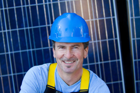 Close up of a Man in his forties overseeing a Solar Instalation with Solar Panels behind him