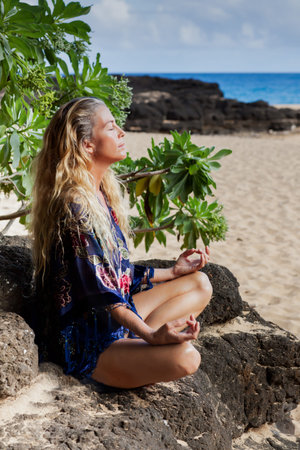 Pretty Woman with long hair in her Forties Meditating in Hawaii on a Lava bed at the Beach