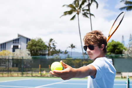 Teenage Boy shows determination serving the tennis Ball in  Hawaiiの写真素材