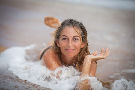 Smiling Woman lying in the surf with sandy wet hairの写真素材