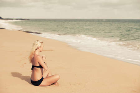 Beautiful Blonde sitting in the Quiet of the Beach in prayer poseの写真素材