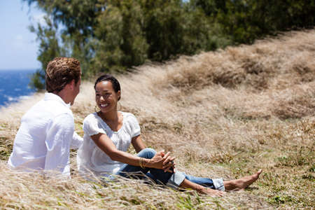 Good looking couple sitting in tall grass on a bluff above the ocean in Hawaiiの写真素材