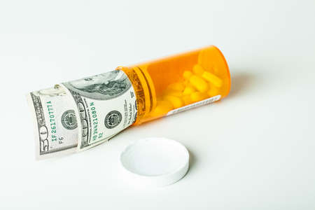 Prescription Drugs in a container with a hunderd dollar bill and a fifty isolated on whiteの写真素材