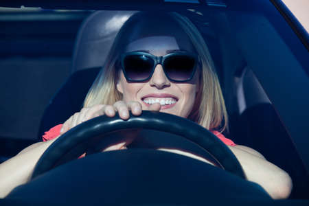 Pretty blonde woman behind steering wheel of a sports car with a big smileの写真素材