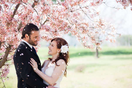 Beautiful happy bride and groom being showered with confetti from cherry blossomsの写真素材