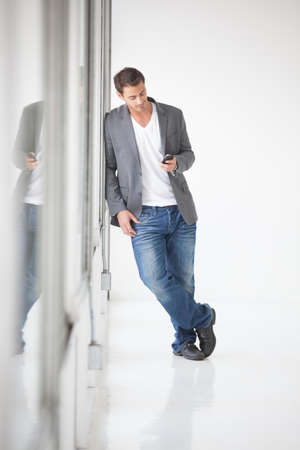 Gorgeous young man leaning on a glass wall and textingの写真素材